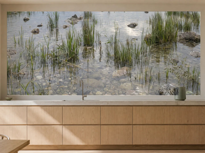 Küchenrückwand „Schilf und helle Kiesel im Flachwasser“ als installierte Rückwand in einer warmen Küche