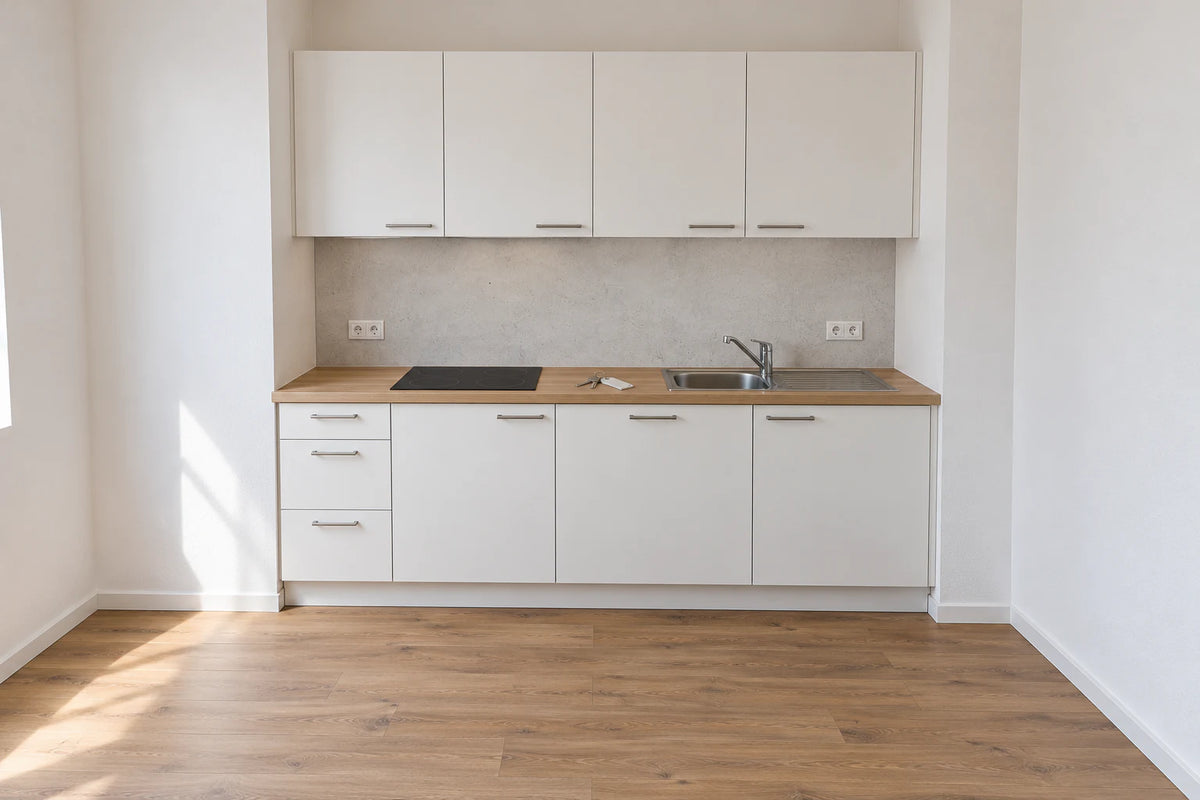 Visualisierung: Leere Mietküche mit hellgrauer Beton-Rückwand, zwei Steckdosen in der Rückwand und Wohnungsschlüsseln auf der Arbeitsplatte